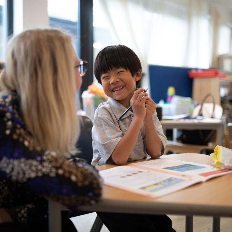 a young smiling school boy sitting at a desk with teacher